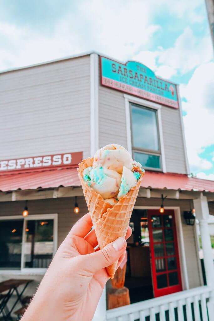 A woman's hand holds a waffle cone filled with rainbow colored ice cream.