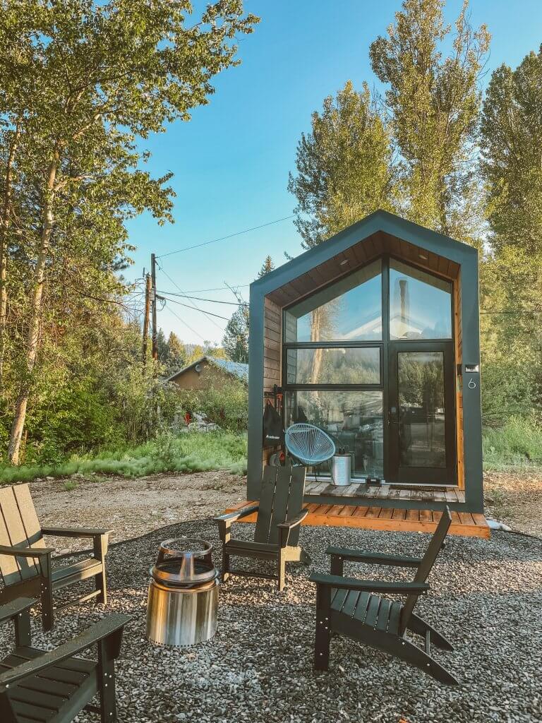 Exterior shot of a tiny home cabin with floor to ceiling windows and a chair and fire pit in the foreground at Smoke Jumper Tiny Resort in Idaho City.