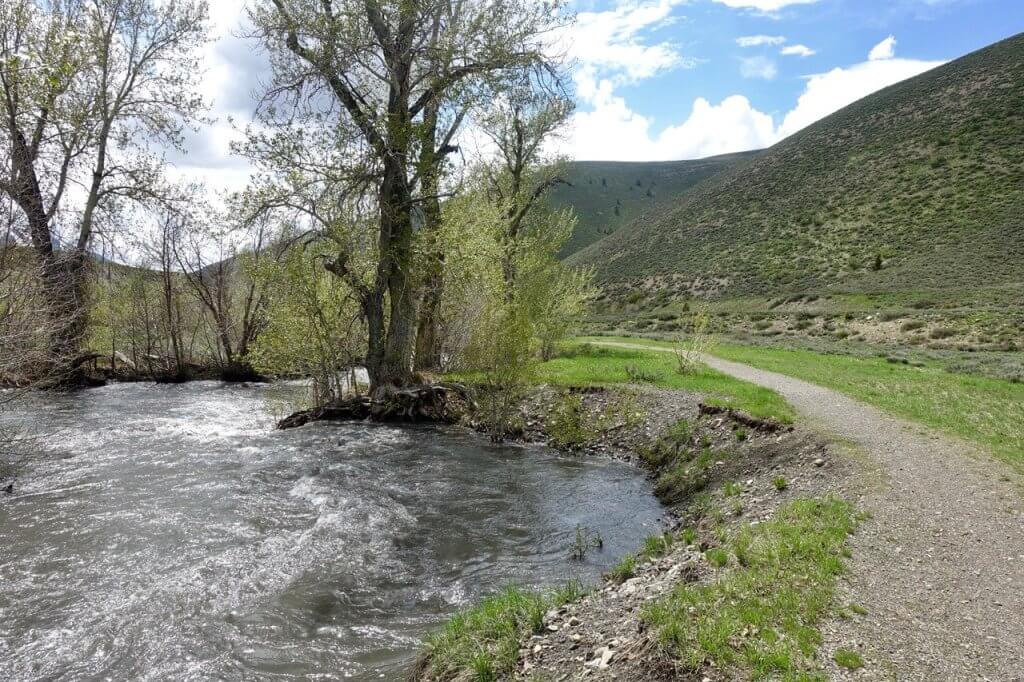 A compact gravel trail runs alongside a full mountain creek.