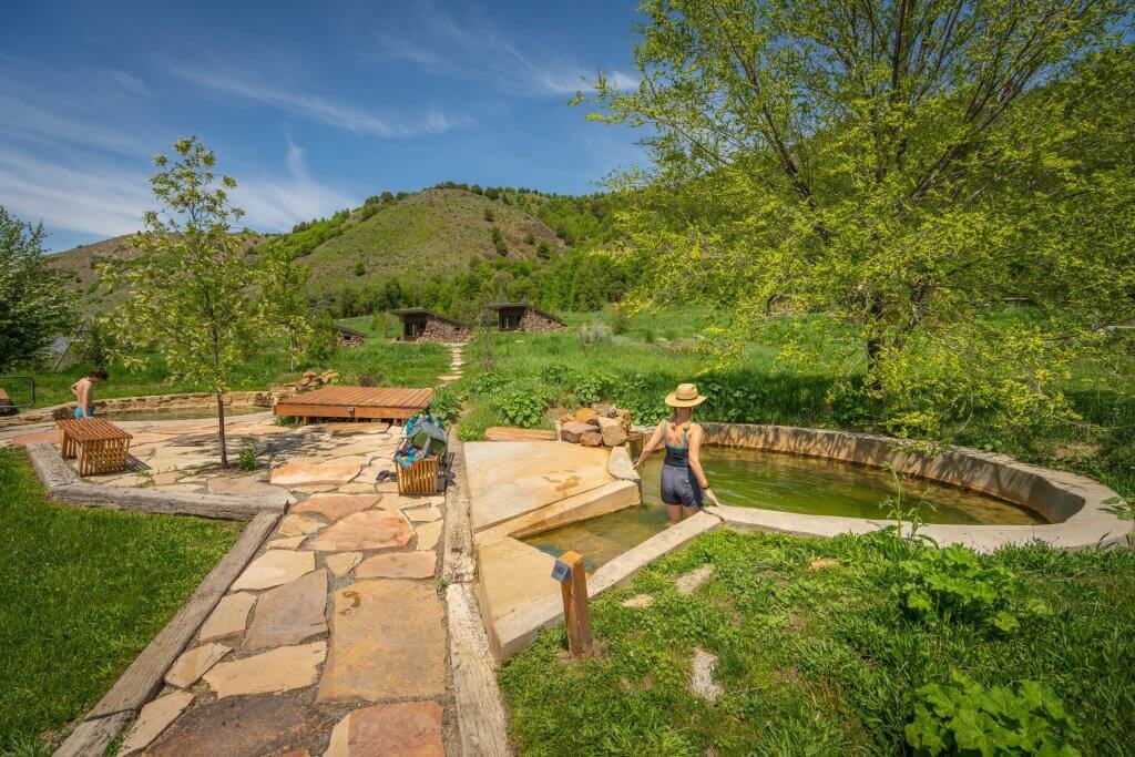 A woman and child approach a developed hot spring pool from a landscaped path.