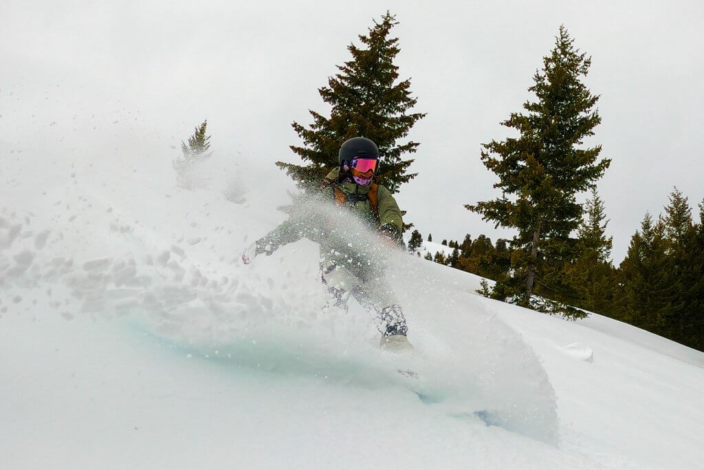 A person in snow gear skiing down a slope at Soldier Mountain Ski Area in front of alpine trees.