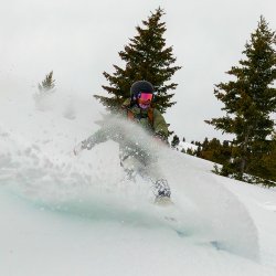 A person in snow gear skiing down a slope at Soldier Mountain Ski Area in front of alpine trees.