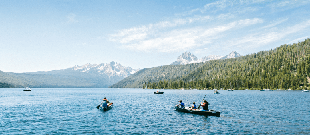 Groups of people kayaking on Priest Lake, with a forest and mountains in the distance.