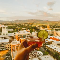 A cocktail held in a hand and a view of the Boise skyline in the background at Ampersand.