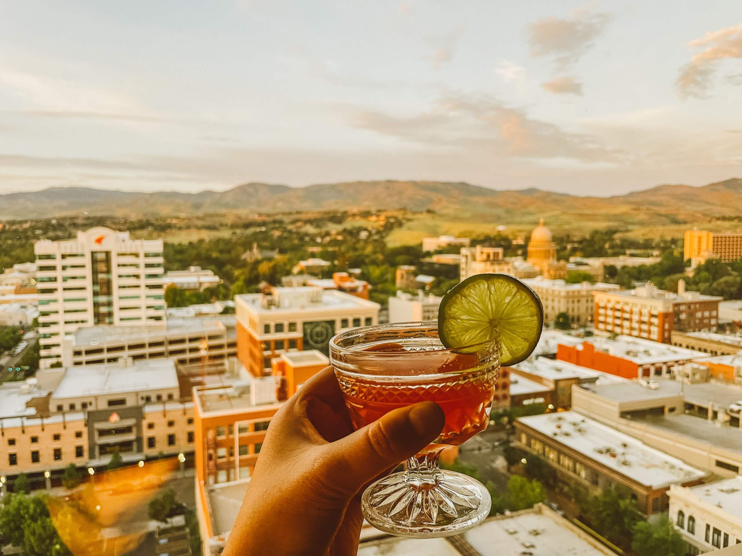 A cocktail held in a hand and a view of the Boise skyline in the background at Ampersand.