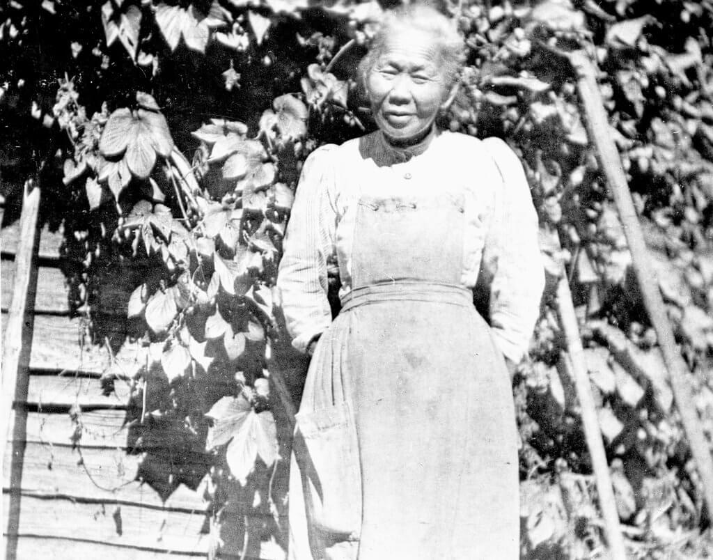 A black-and-white photo of Polly Bemis standing in front of the cabin.