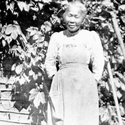 A black-and-white photo of Polly Bemis standing in front of the cabin.