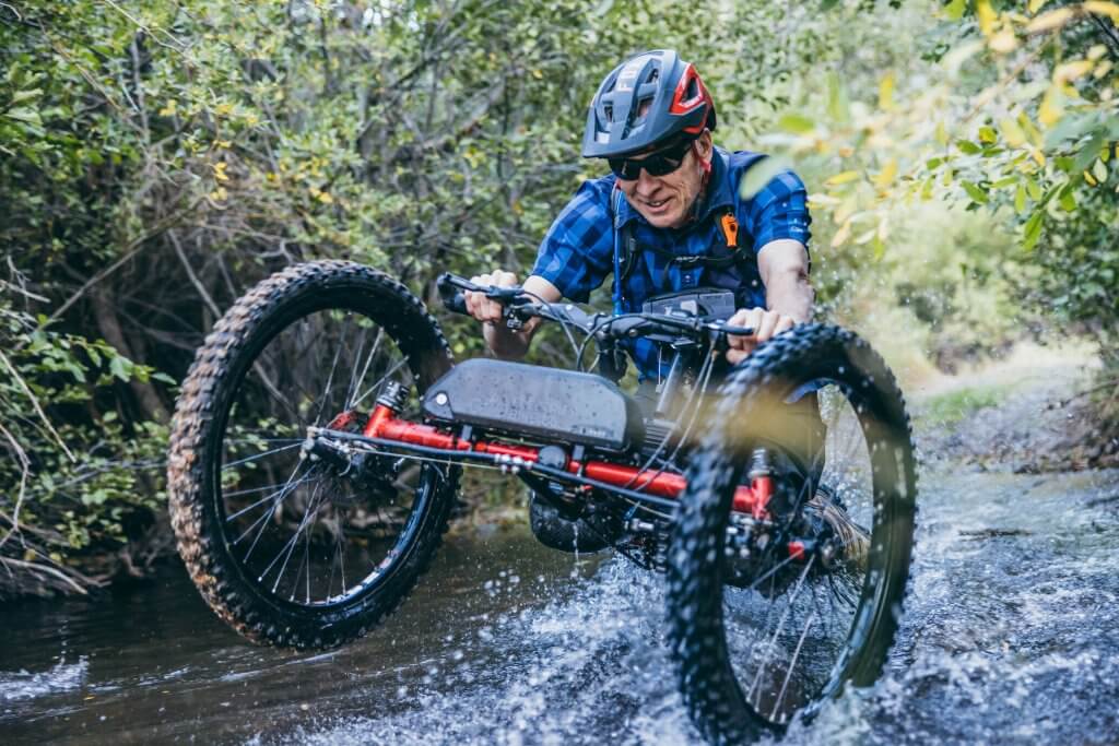 Idaho. Beyond Words. A man riding an accessible bike through the shallow waters of Agency Creek.