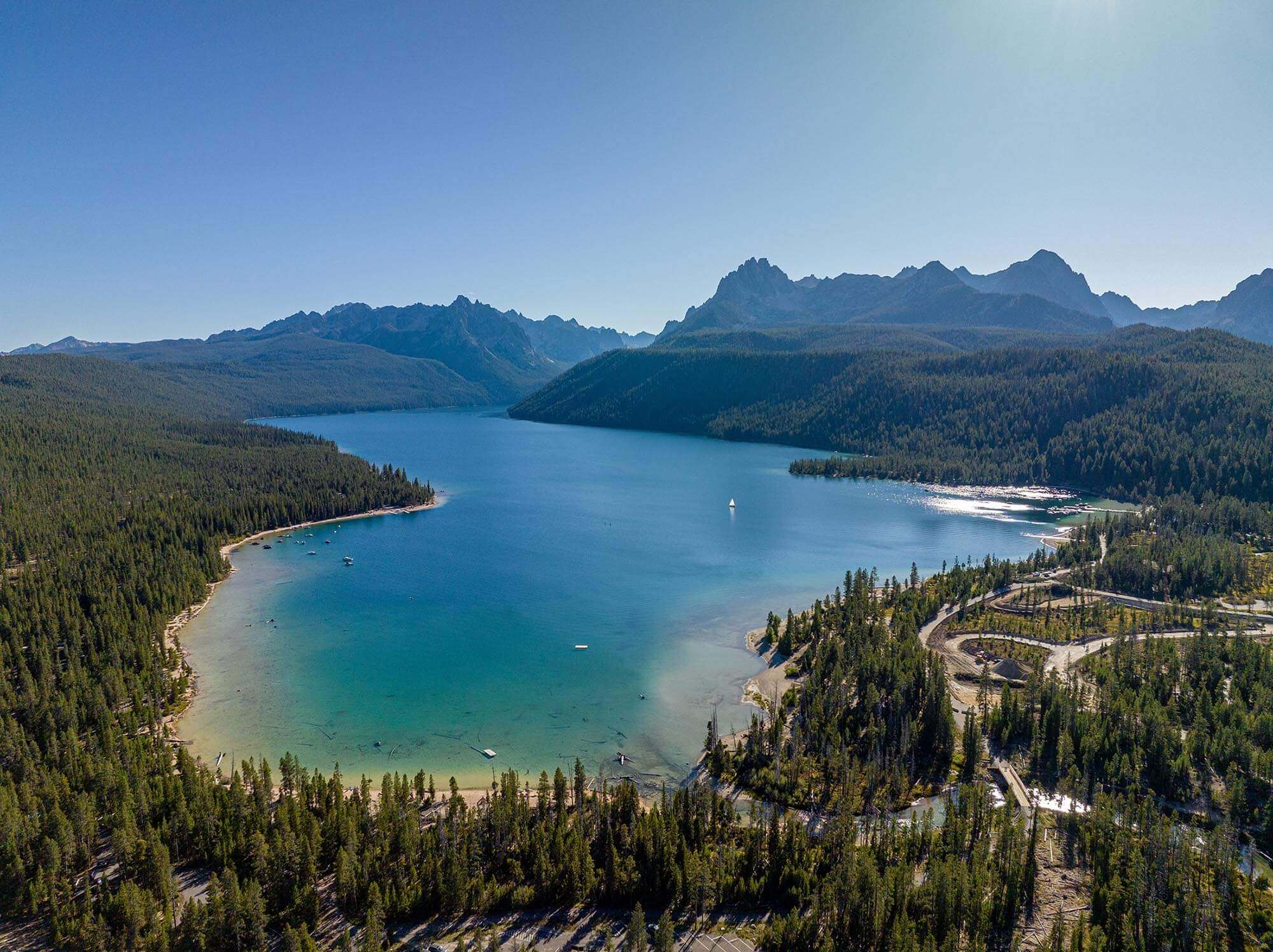 An overhead view of a blue lake surrounded by forest and mountains.