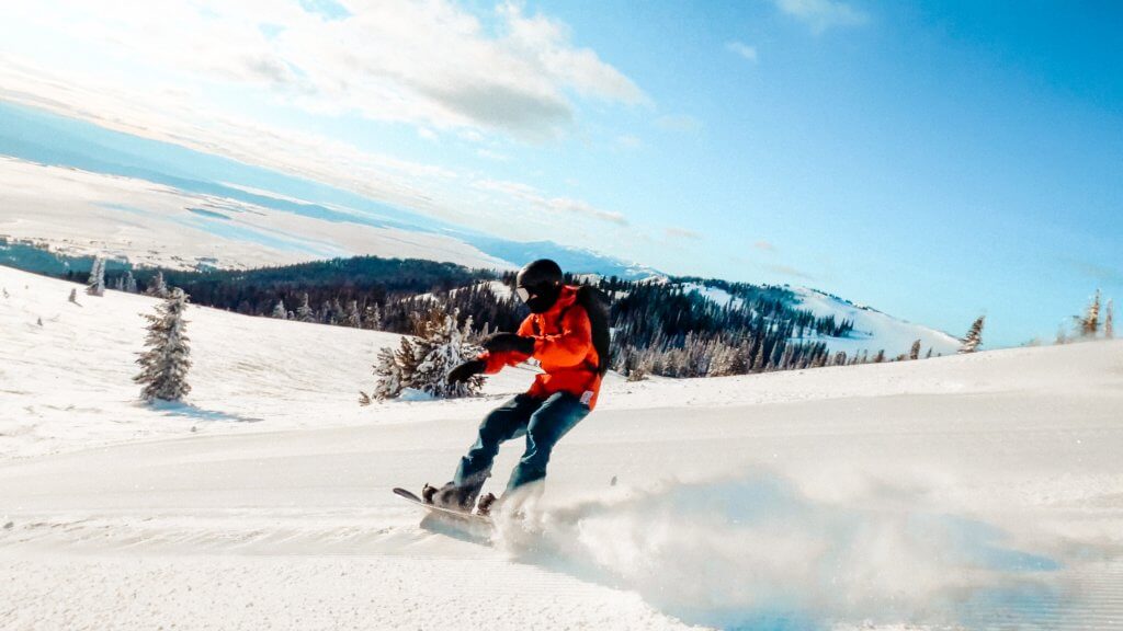 A snowboarder in a red jacket glides down a slope at Tamarack Resort. 