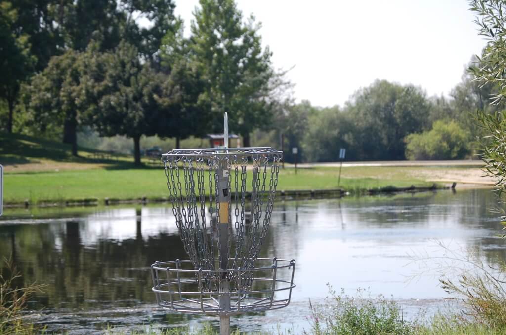 A disc golf basket with a lake in the background at Eagle Island State Park.