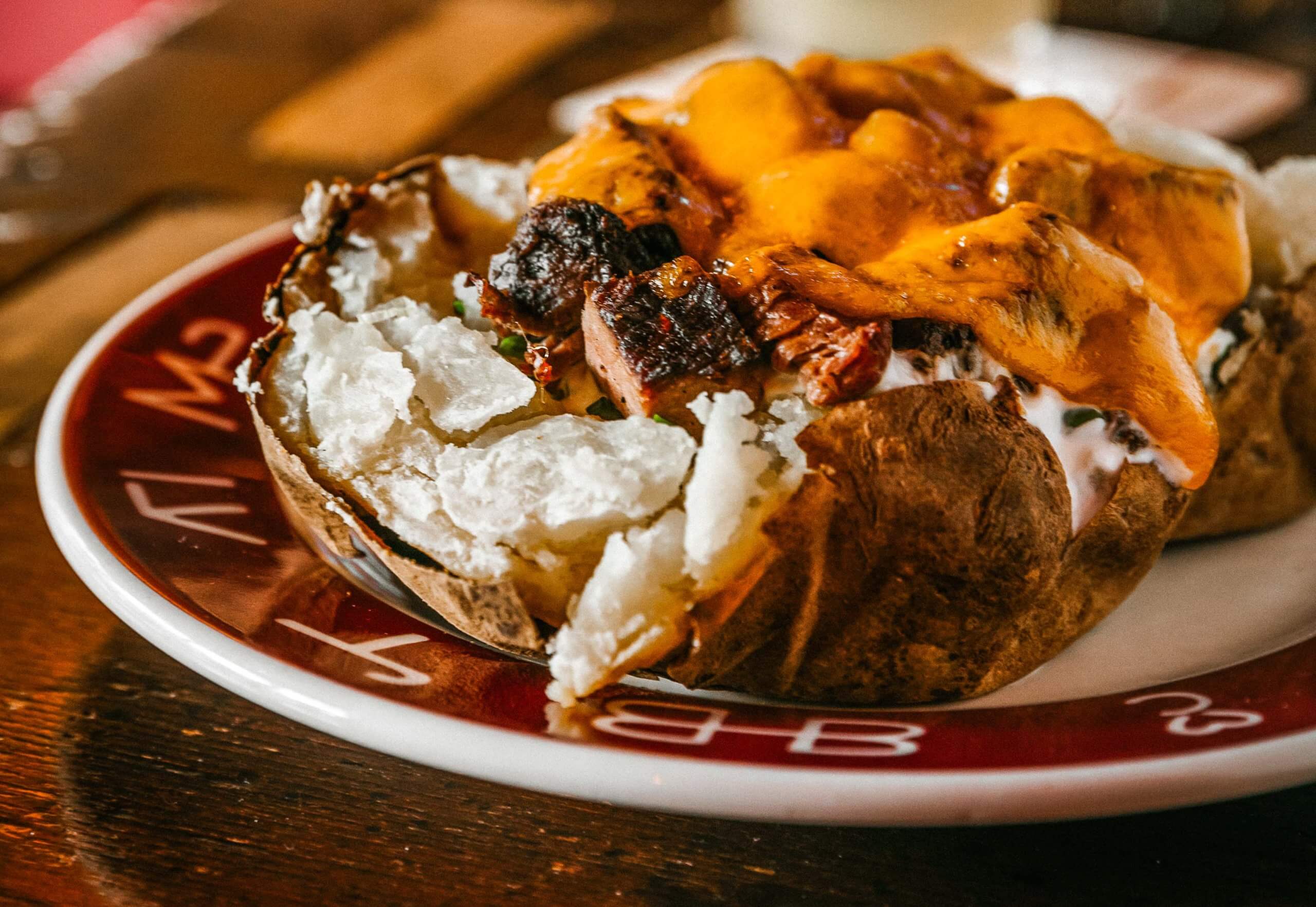 A giant baked potato stuffed with butter, sour cream, caramelized onions, chives and diced teriyaki beef and smothered in melted cheese called a Jim Spud on a plate.