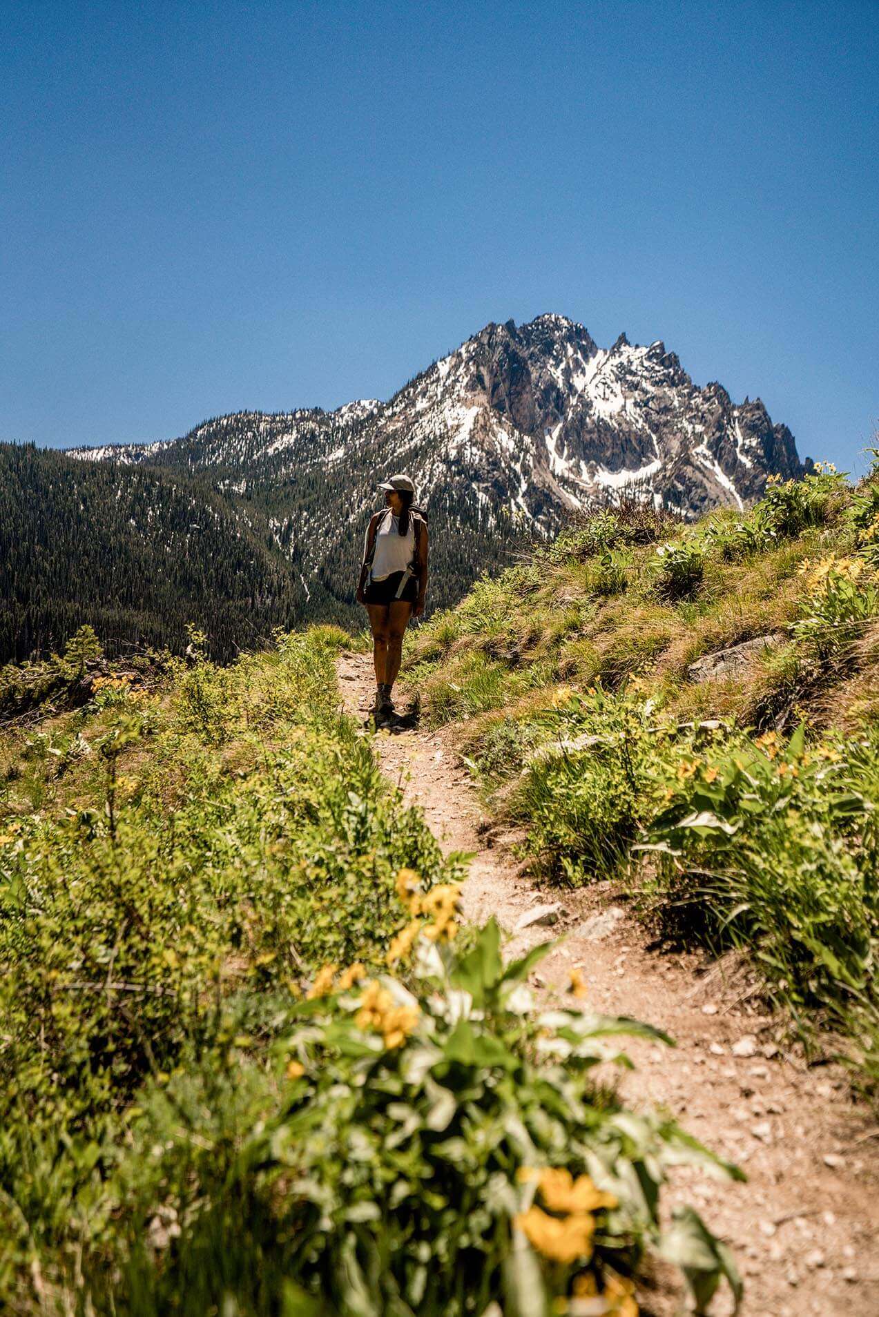 A woman hiking along the Bench Lakes Trail and snow-capped mountains in the distance.