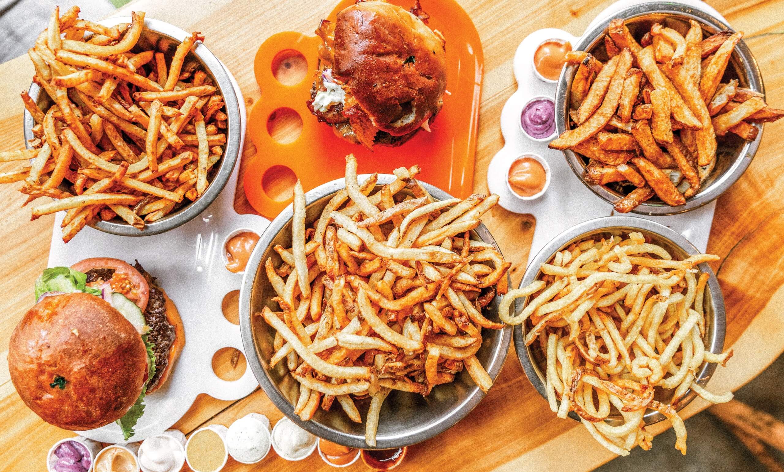 An overhead view of four bowls of fries and two burgers on a table at Boise Fry Co.