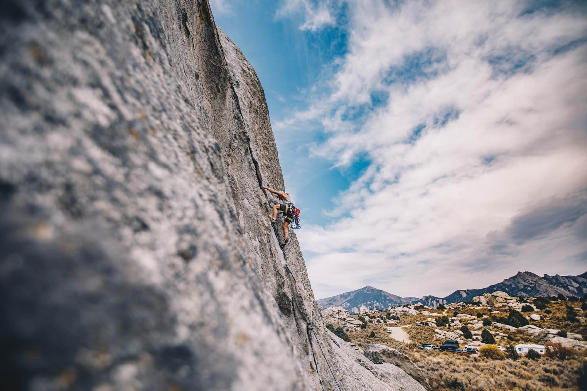 A person climbs up a large rock face with a scenic rocky landscape in the distance.