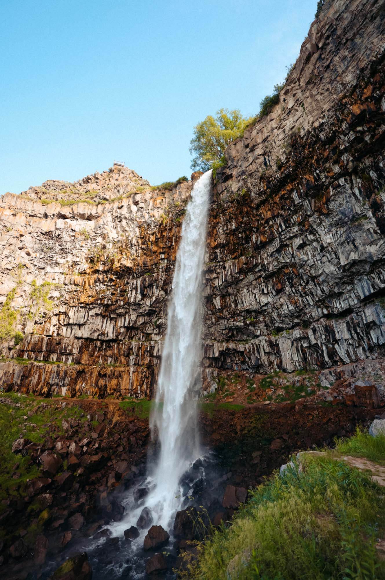 A waterfall flows out from a large rock wall onto rocks below.