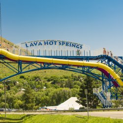 Water park visitors walk up stairs to access two waterslides near a sign that says Lava Hot Springs with a mountain in the background.