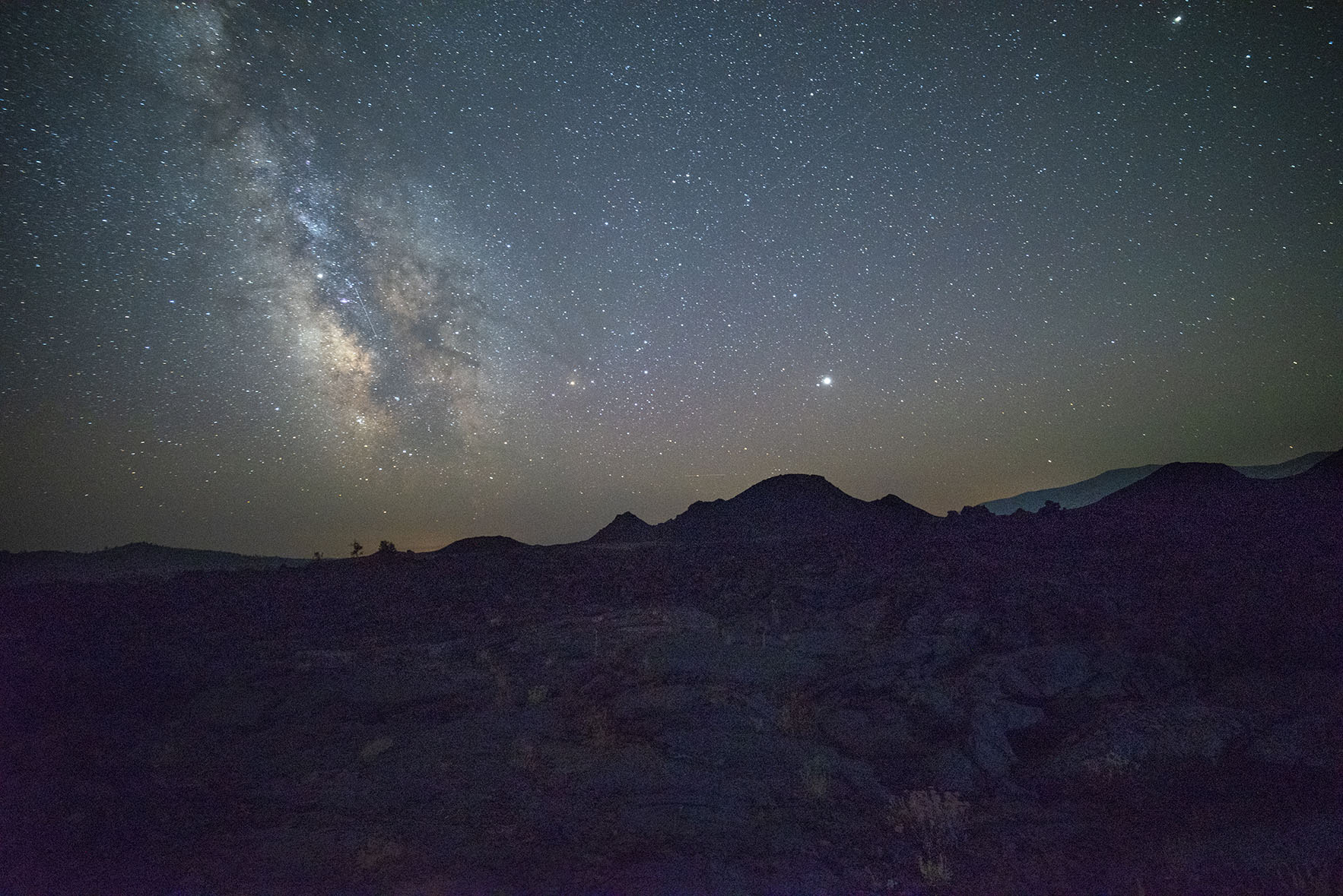 A rolling landscape under a starry dark night sky.