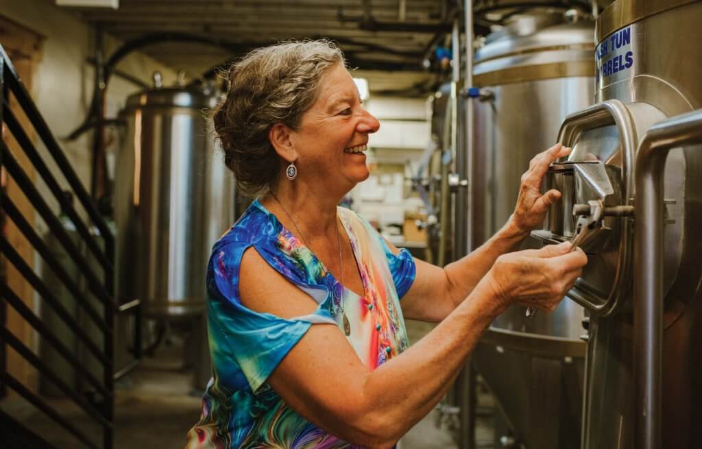 A woman touching beer brewing equipment.