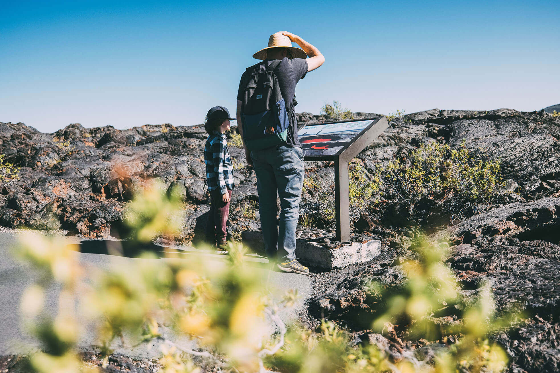 A father and child look over an interpretive sign along a trail surrounded by lava rock.