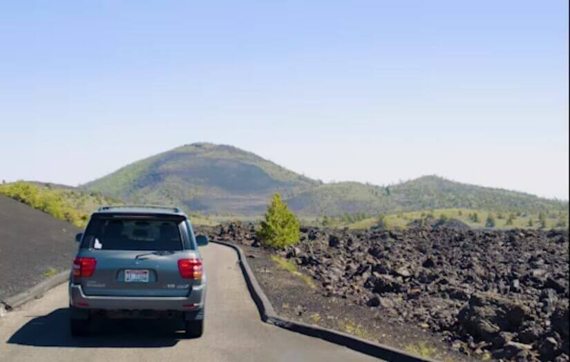 A still from a video of a vehicle driving on a paved road through a field of lava rock formations.