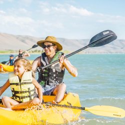 A father and daughter kayaking on a Bear Lake with mountains in the distance.