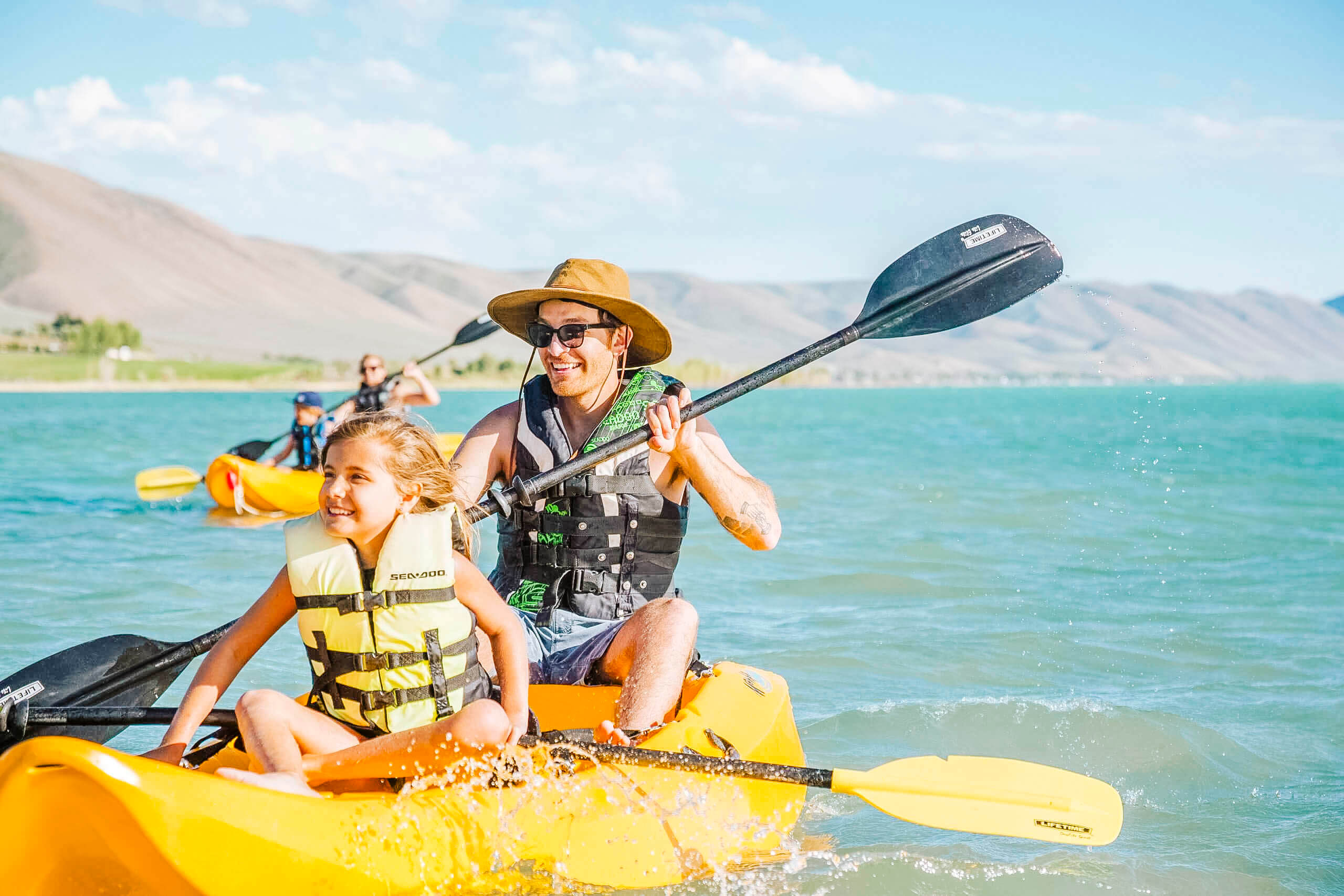 A father and daughter kayaking on a Bear Lake with mountains in the distance.