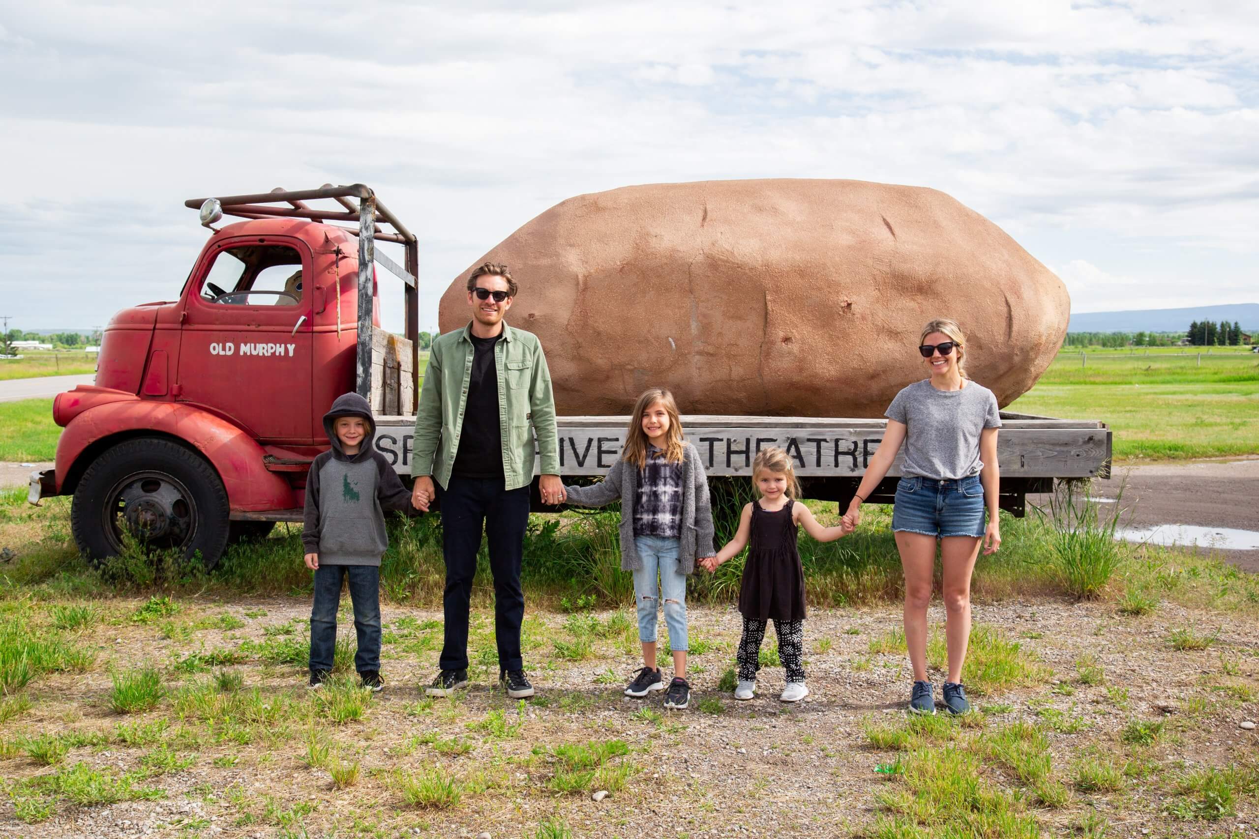 A family of two and adults and three small children standing in front of a truck carrying a giant potato at the Spud Drive-In.