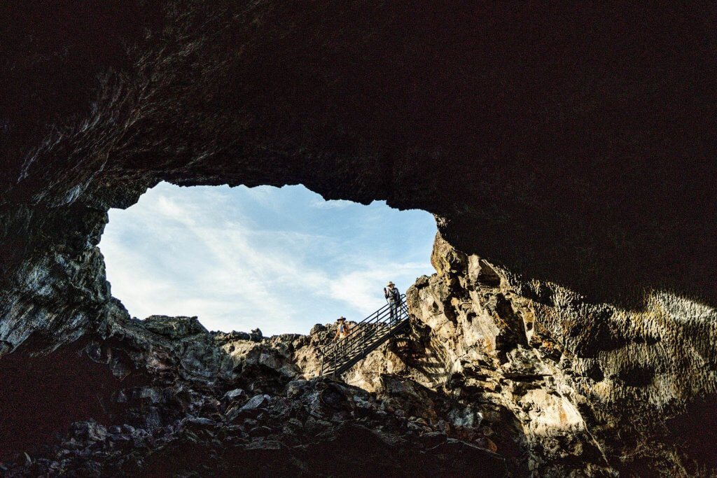 Two people on a staircase looking into Indian Tunnel cave at Craters of the Moon.