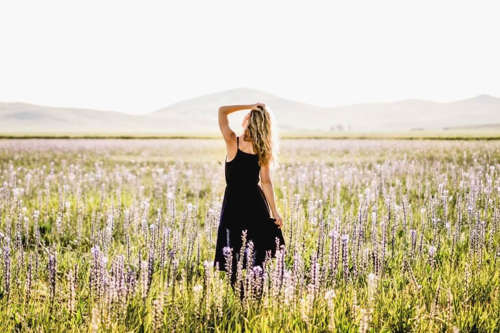 A woman stands with her hand in her hair in a sunlit field at Camas Prairie Centennial Marsh Wildlife Management Area, mountains in the distance.