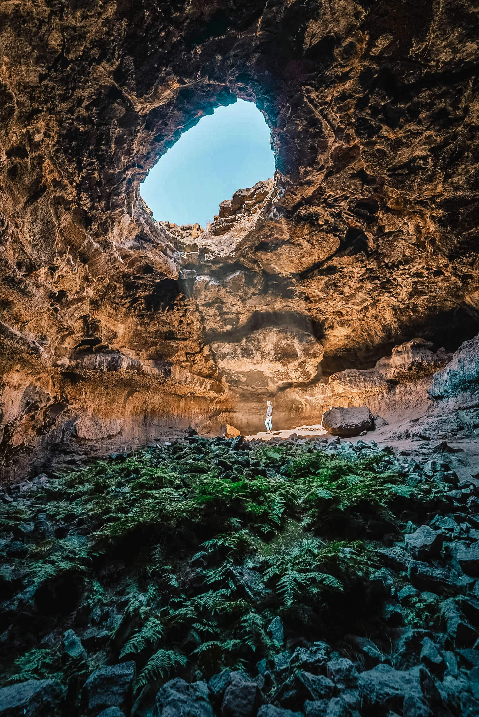 A person inside in Tea Kettle Cave, standing in the light streaming through a large hole at the top of the cave.