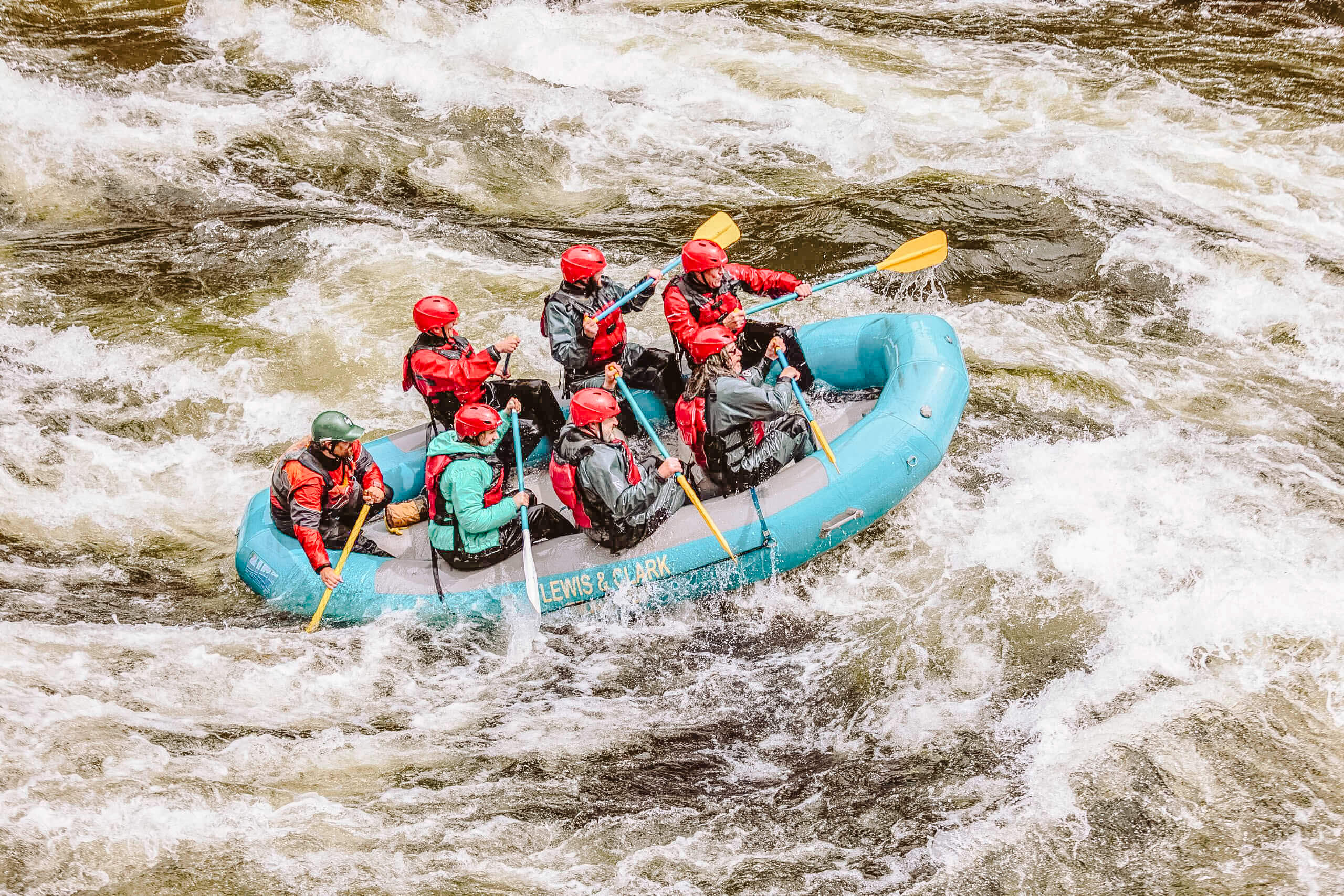 Seven people with red helmets sit in a blue raft for whitewater rafting.