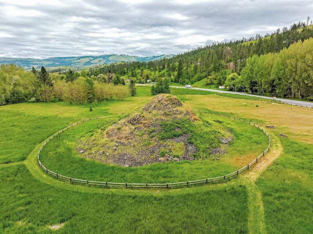 An aerial view of the Heart of the Monster site, surrounded by a sprawling field and a tree-covered hill off the side.