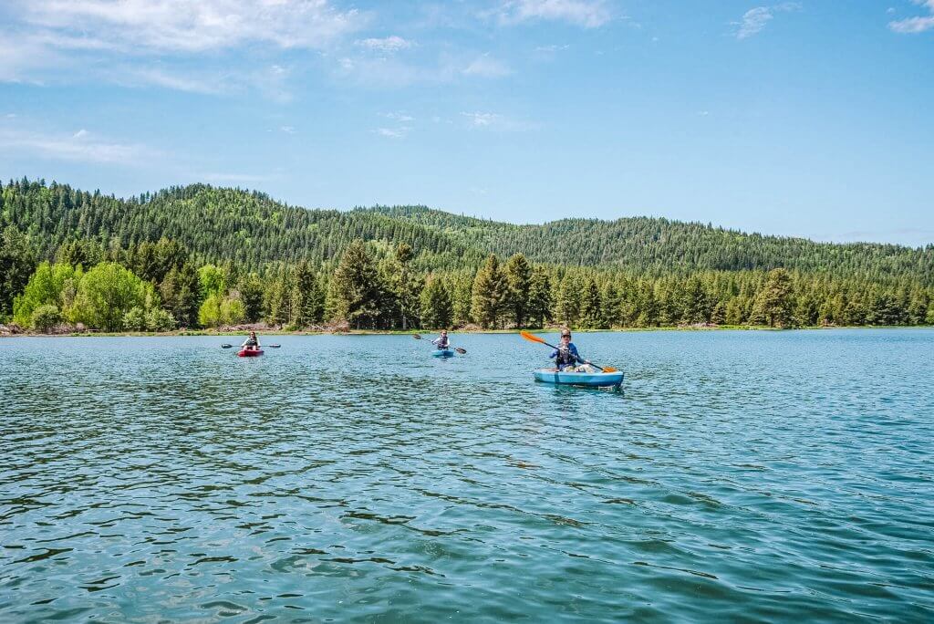 Three people kayaking at Spirit Lake, with tree-covered hills in the background.