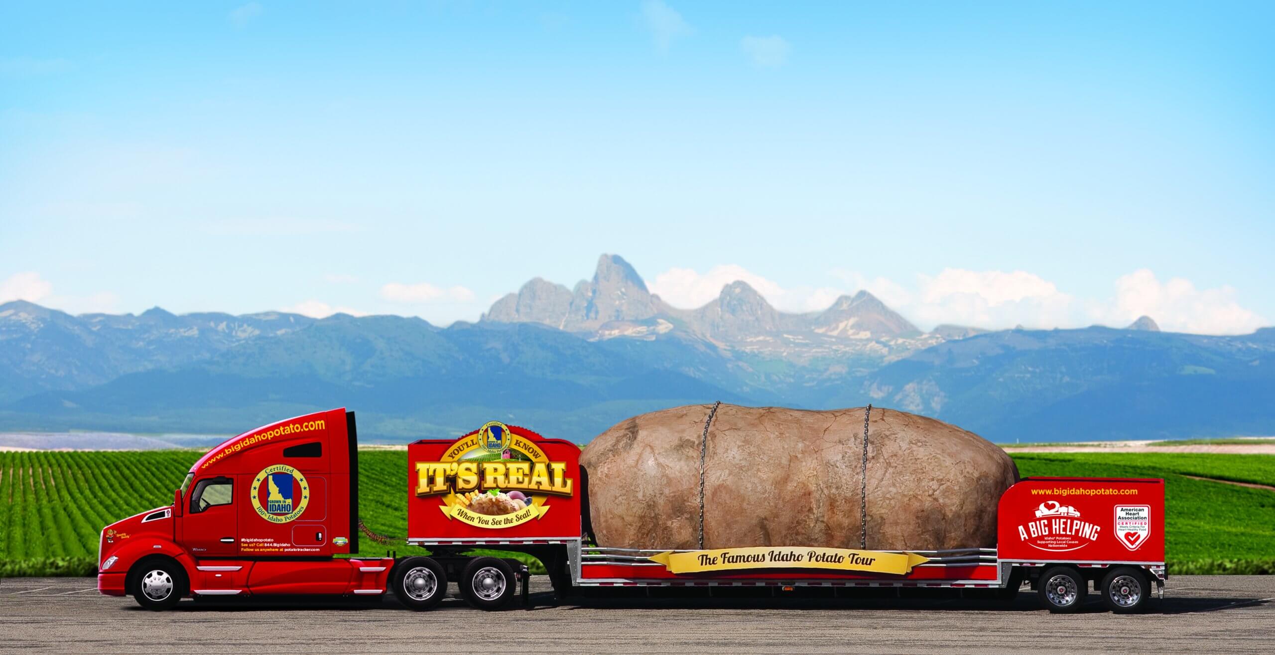 A red semi truck called the Big Idaho Potato Truck carrying a 4-ton potato and sprawling field and mountains in the background.