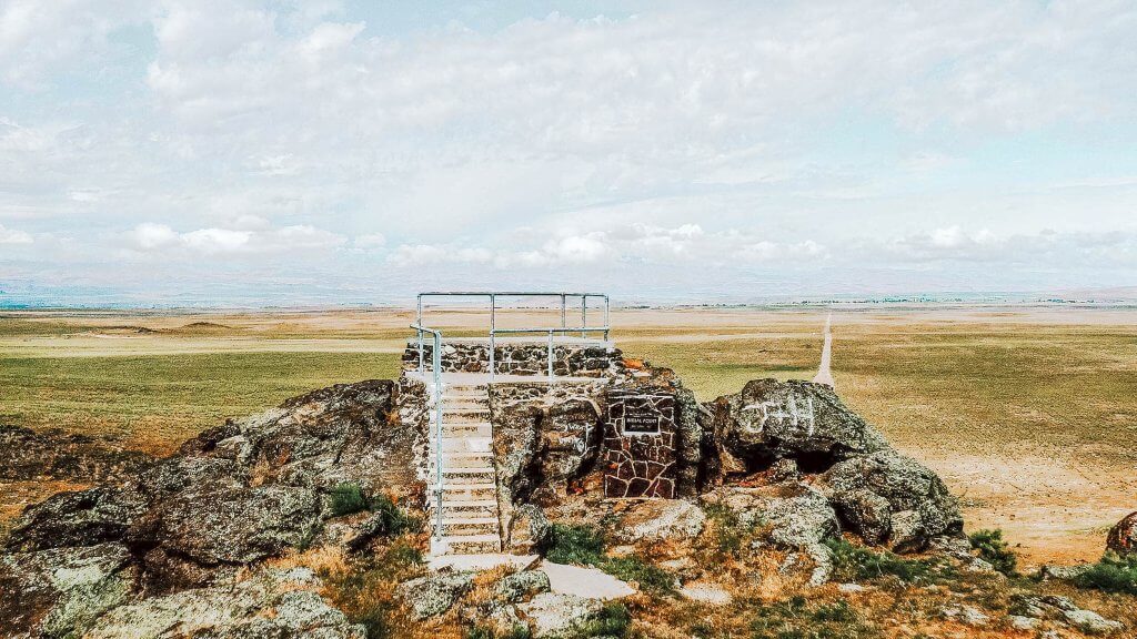 Historic stone steps with a metal hand rail overlooking an open landscape.