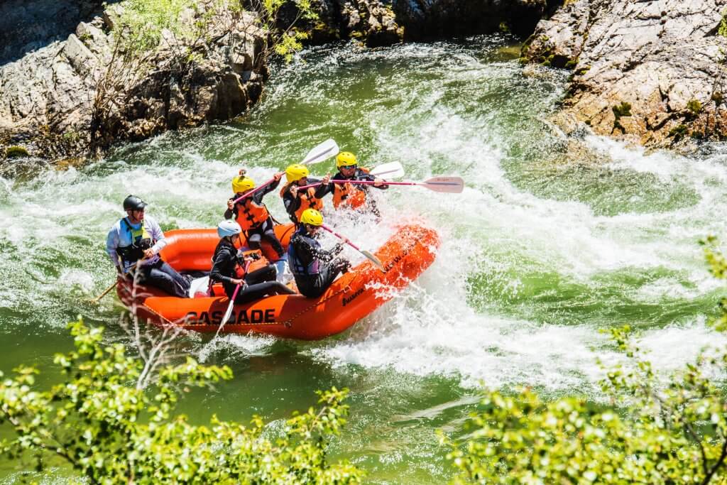 A group goes whitewater rafting in helmets across the South Fork of the Payette River as rapids rush and splash around them.