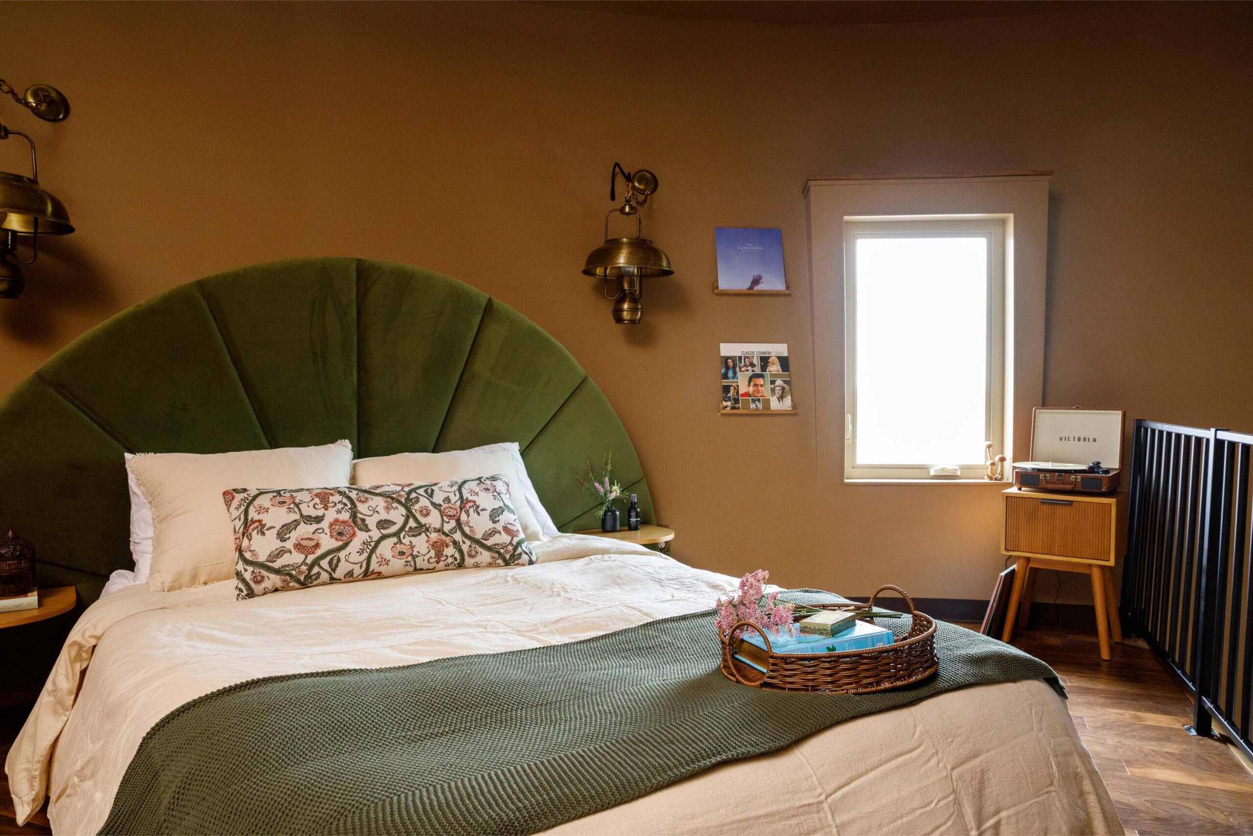 A view of the luxe master bedroom inside The Flower Pot in Burley, where a velvet green headboard leans against the wall as a pillow with blooms sits against it.