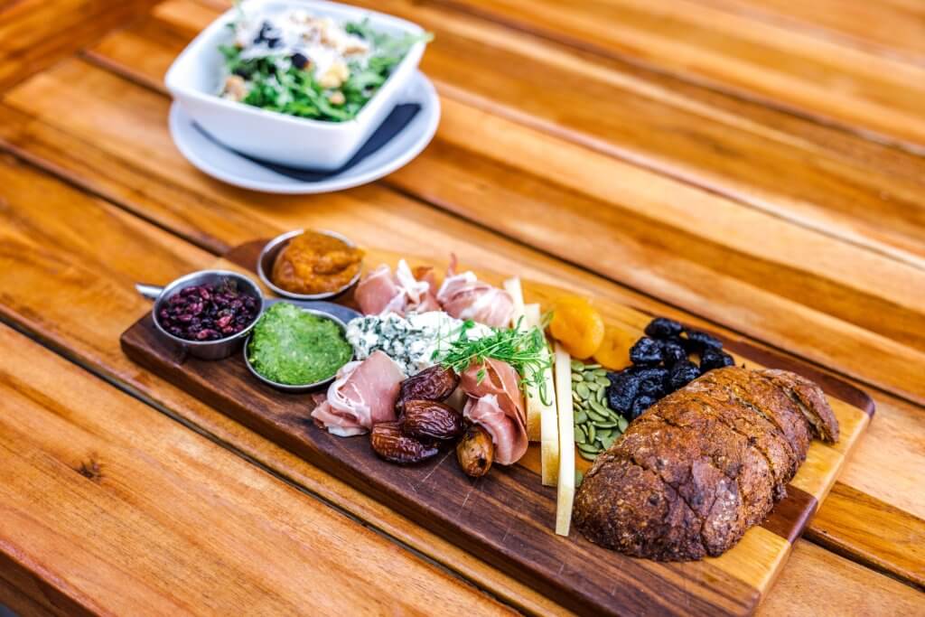 A charcuterie board of bread, meat, nuts and dried fruits and a salad in the background at Forage Bistro and Lounge.