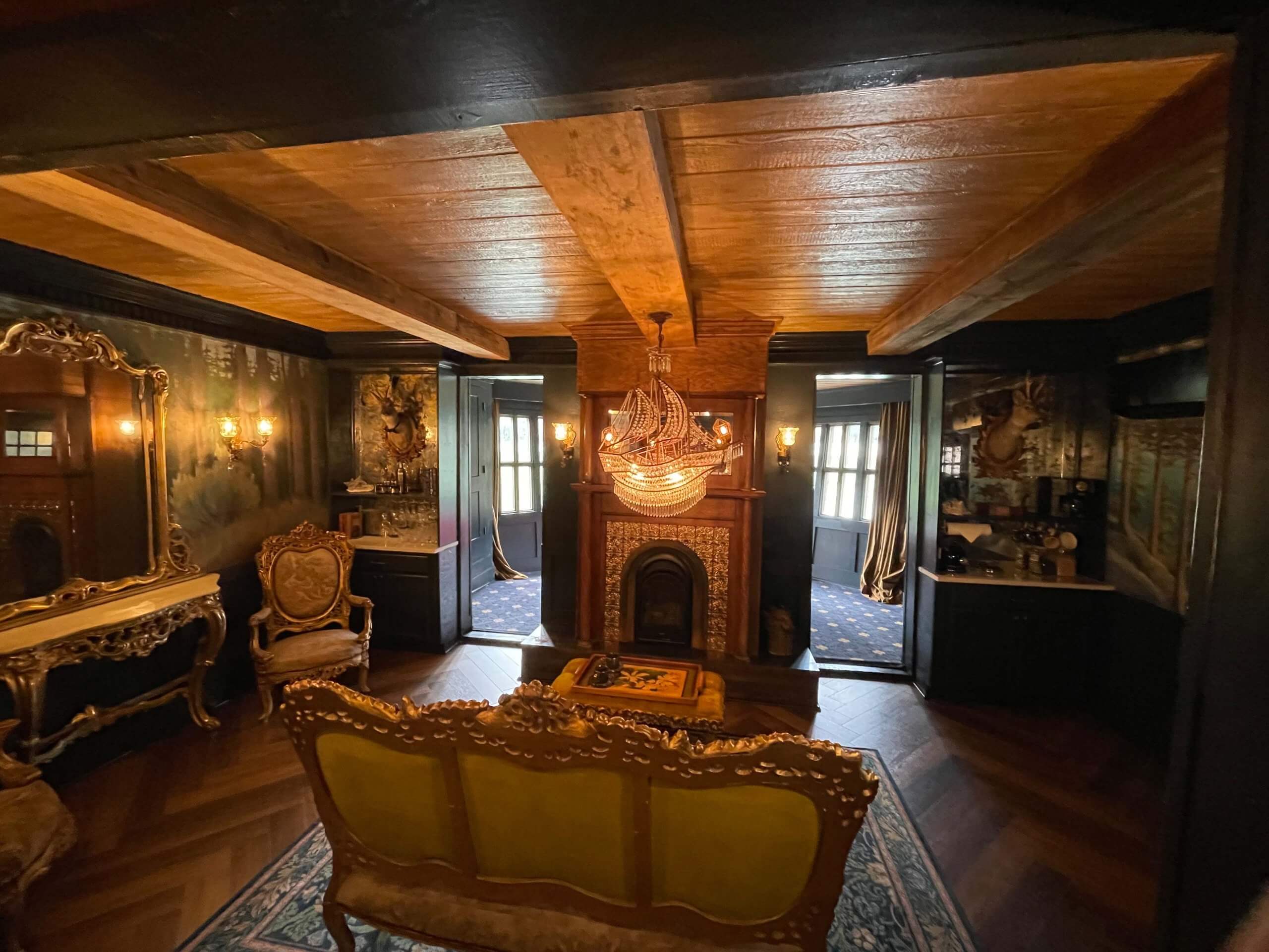 A look inside the Shipwreck House in Salmon, Idaho, where a ship chandelier hangs glowing from the wooden ceiling. The house features beautiful green and gold furniture, a large mirror, and painted walls.