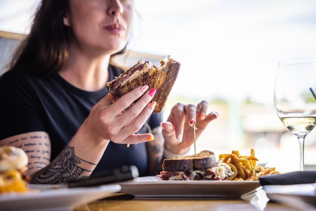 A woman seated at a table enjoying a sandwich, fries and a glass of wine at The Settlement Kitchen + Craft Tavern.