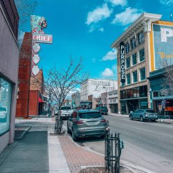 Cars parked on a street lined with historical buildings and neon signs in downtown Pocatello.