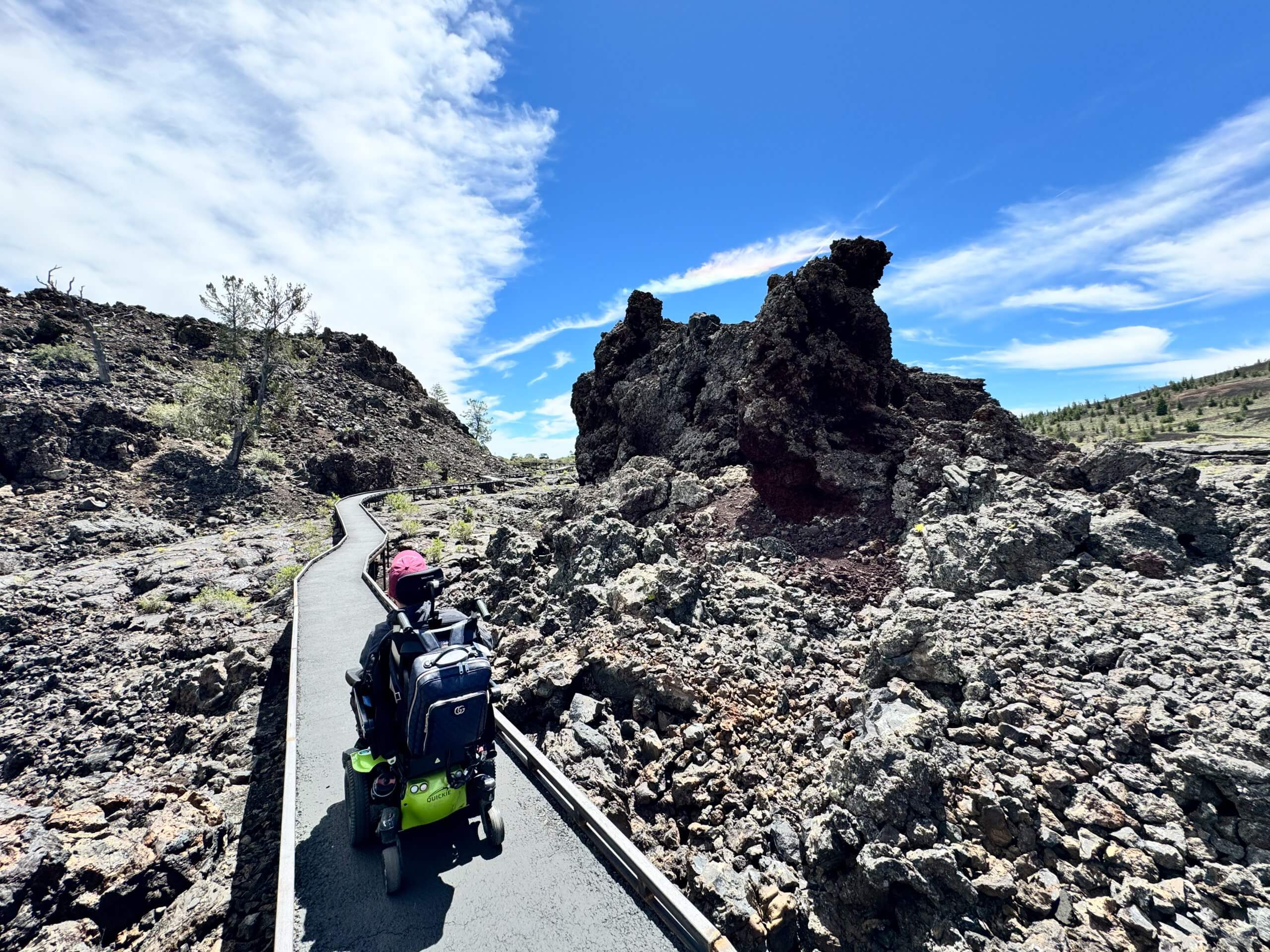 A man in a wheelchair is on a paved path looking at lava formations at Craters of the Moon.