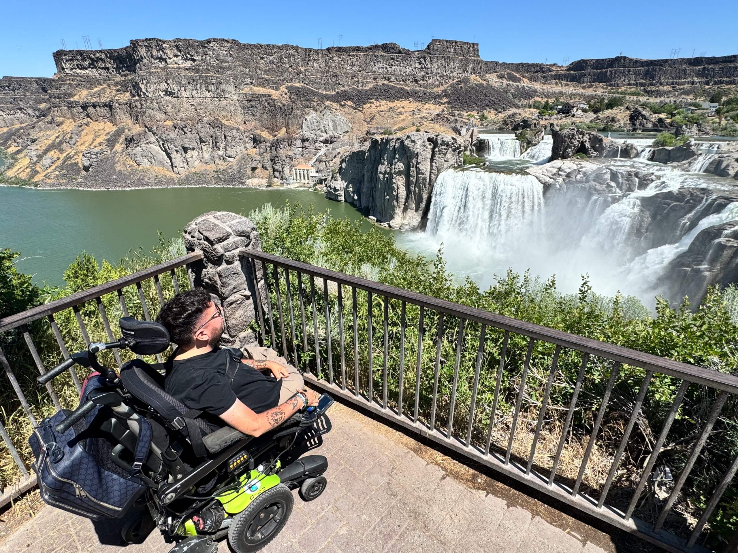 A man in a wheelchair sits on a viewing platform looking at Shoshone Falls in the distance.