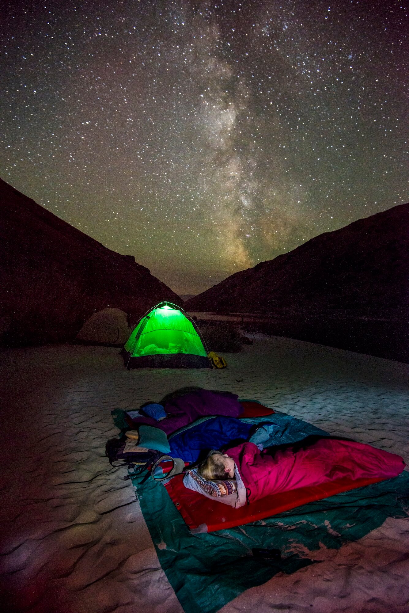 People sleep under the stars in sleeping bags with a galaxy overhead.