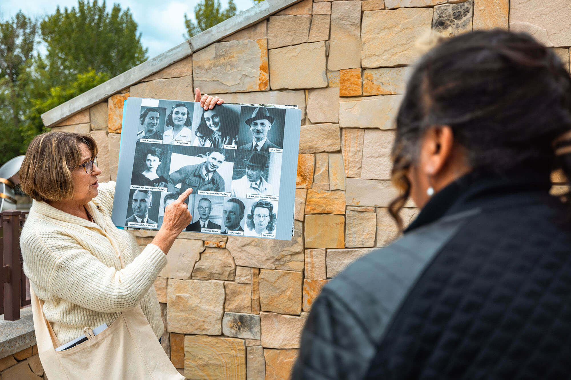 A woman holding and pointing to a poster with a collage of historical images of Anne Frank, her family members and other figures.