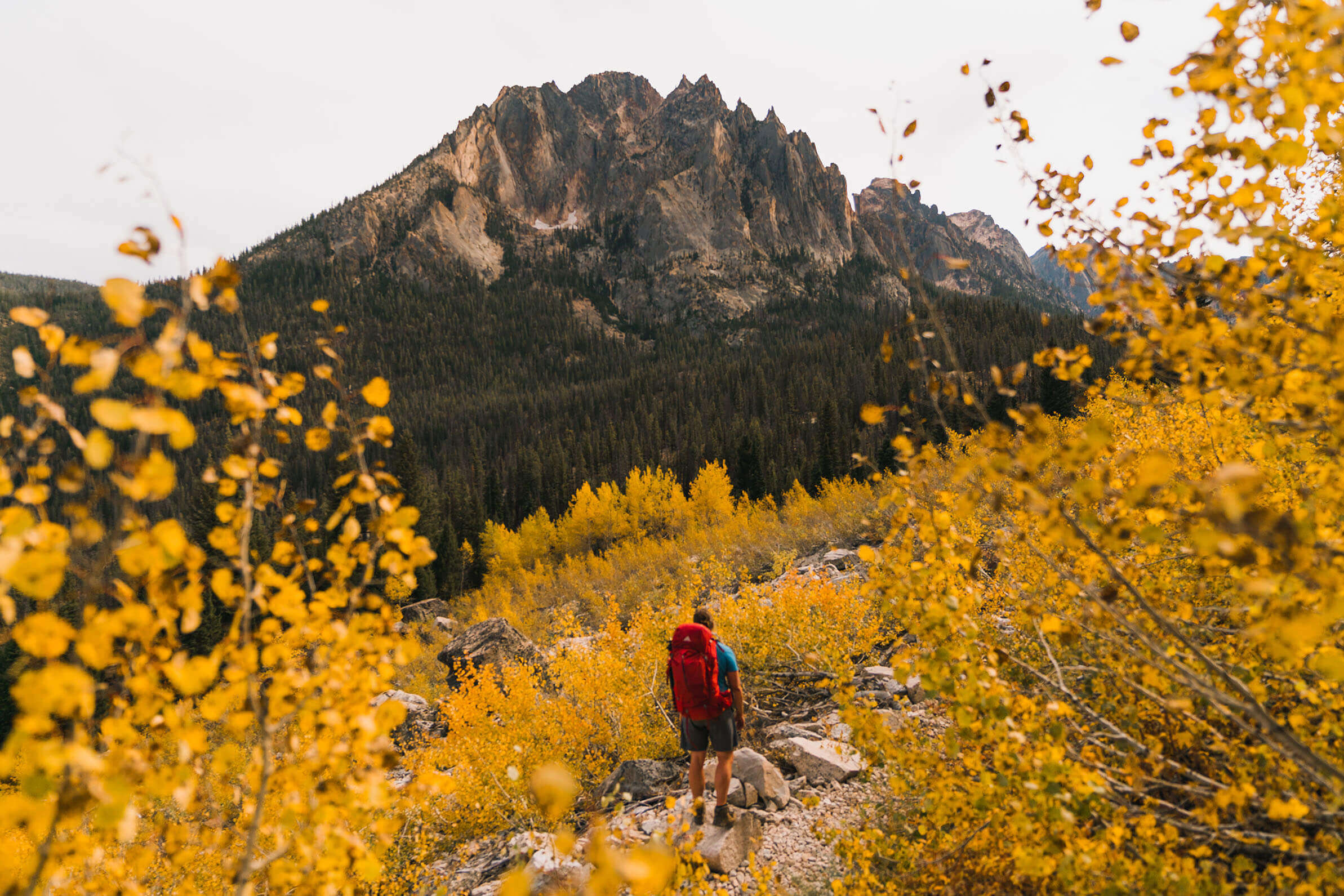 A man wearing a red backpack hikes to Elephants Perch during fall in the Sawtooth Mountains near Stanley.