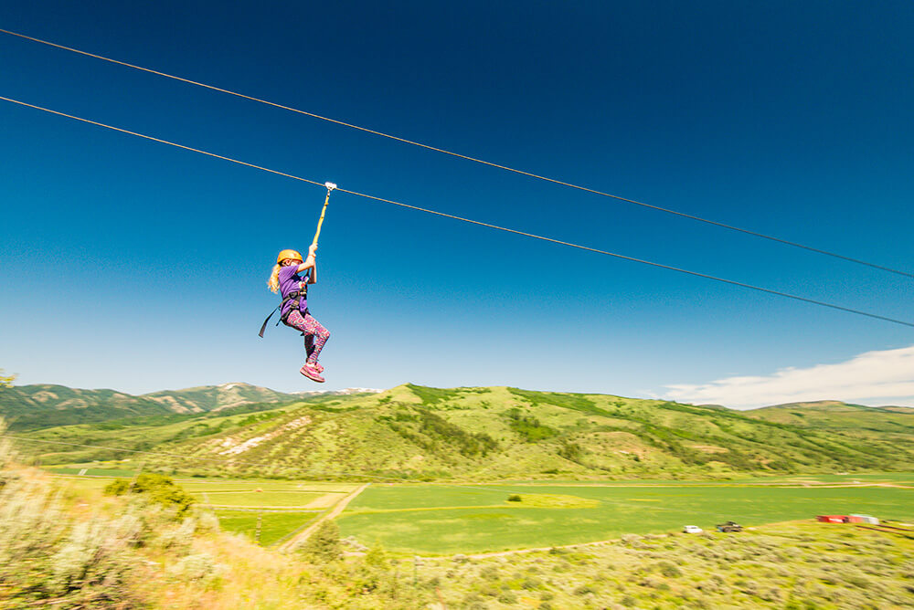 A child ziplining over a wide open, green landscape with green mountains in the distance at Lava Zipline.