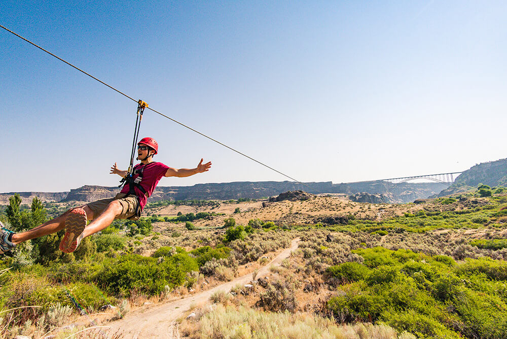 A man ziplining with his arms and legs outstretched through the Snake River Canyon and the Perrine Bridge in the background at AWOL Adventure Sports Zipline Tours.