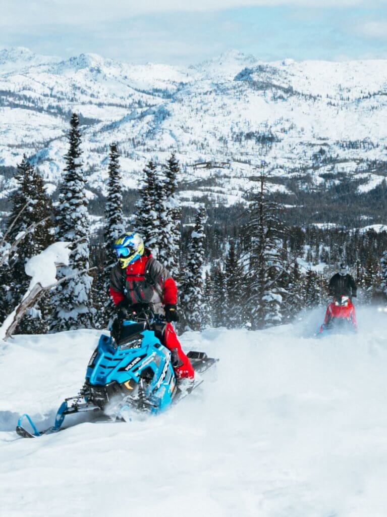 Two people on blue and red snowmobiles traverse a winter trail at Brundage Mountain Resort.